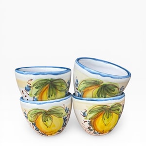 May include: A stack of four ceramic bowls with a hand-painted lemon design. Each bowl features a yellow lemon with green leaves and blue accents on a cream background. The rims are trimmed with a blue border.