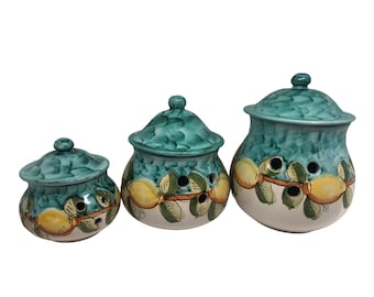Peut inclure: Ensemble de trois pots en céramique avec couvercles, présentant un motif vert et blanc avec des citrons jaunes et des feuilles vertes. Les pots ont des trous sur les côtés pour la ventilation.
