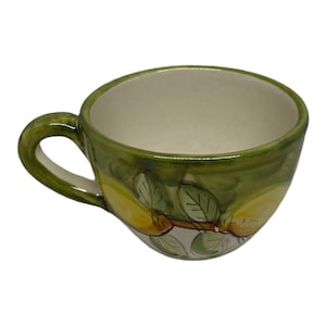May include: A green ceramic teacup with a white interior and a handle. The cup is decorated with a painted design of lemons and leaves.