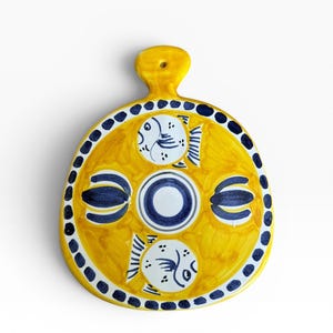 Könnte beinhalten: Eine gelbe Keramik-Servierplatte mit Griff. Die Platte hat ein kreisförmiges Design mit blauen und weißen Fischen und einem gepunkteten Rand. Die Mitte hat ein blaues und weißes Kreisdesign.