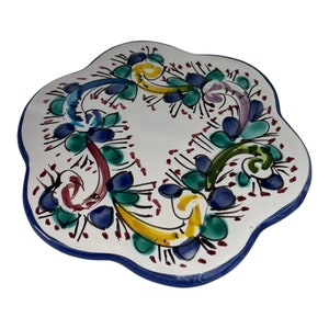 Könnte beinhalten: Ein weißer Keramikteller mit blauem Rand und einem floralen Design in den Farben Blau, Grün, Gelb und Rot.