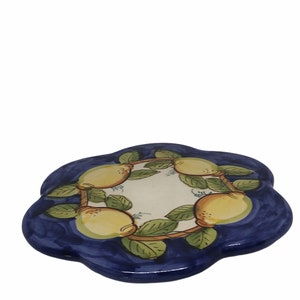 May include: A blue and white ceramic trivet with a flower-shaped design. The trivet is decorated with a wreath of lemons and green leaves.