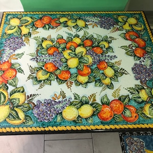 May include: A square table top with a hand-painted design of lemons, oranges, and purple flowers on a white background. The table top has a teal blue border with a yellow rope design.