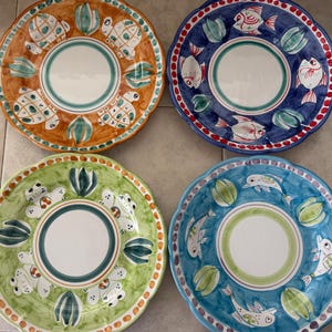 May include: Four decorative ceramic plates with scalloped edges. Each plate features a different design: turtles, fish, and aquatic plants. The plates have a white centre and are painted in shades of orange, blue, green, and white.