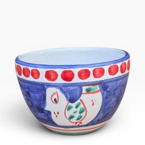 Peut inclure: Un bol en céramique peint à la main, avec un extérieur bleu, représentant un motif d'oiseau blanc avec des accents verts et rouges. Le bord présente un motif de points rouges sur fond blanc. L'intérieur est blanc.