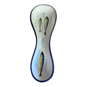 May include: A ceramic spoon rest with a white background, blue trim, and a whimsical fish design. The spoon rest features three yellow and blue fish illustrations and light blue water-like accents.