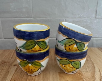 Op de afbeelding: Een set van vier keramische kommen met een handgeschilderd ontwerp van gele citroenen met groene bladeren. Elke kom heeft een brede donkerblauwe rand en een witte binnenkant. De kommen zijn gerangschikt in twee stapels van twee stuks.