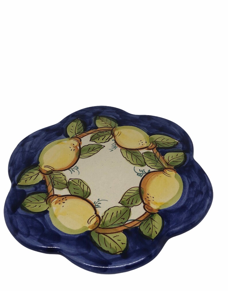 May include: A blue ceramic trivet with a white center and a design of lemons and leaves. The lemons are yellow with green leaves and brown branches.