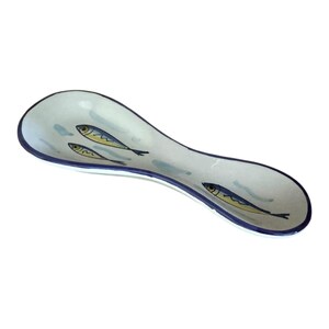 May include: A white ceramic spoon rest with a blue rim and three stylized fish illustrations. The fish are yellow and blue, and the spoon rest has a curved, elongated shape.