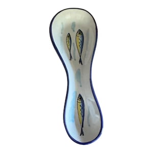 May include: A ceramic spoon rest with a white background and a blue rim. The spoon rest features three yellow and blue fish illustrations. The design is simple and elegant, perfect for any kitchen.