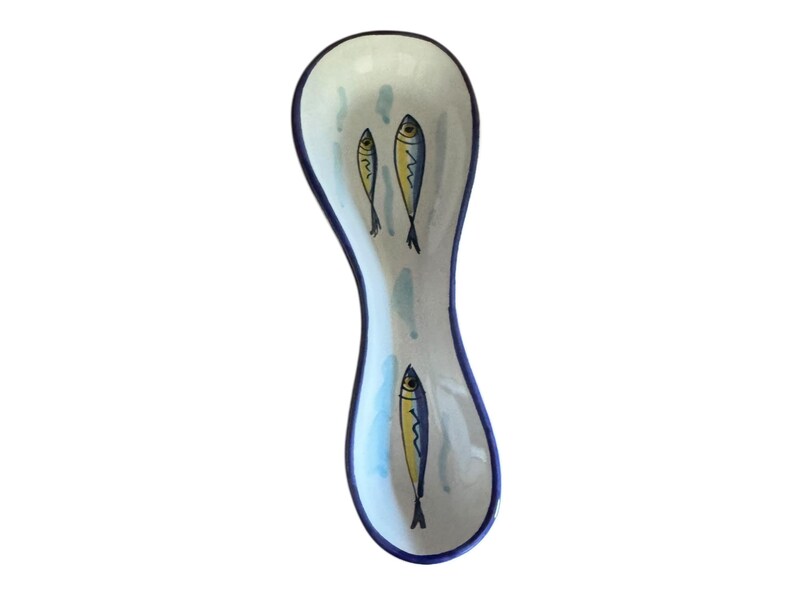 May include: A ceramic spoon rest with a white background and a blue rim. The spoon rest features three yellow and blue fish illustrations. The design is simple and elegant, perfect for any kitchen.