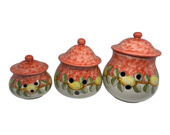 Peut inclure: Ensemble de trois pots de cuisine en céramique avec des couvercles rouges et un motif de citron. Les pots sont de tailles différentes et ont des trous sur les côtés pour la ventilation.