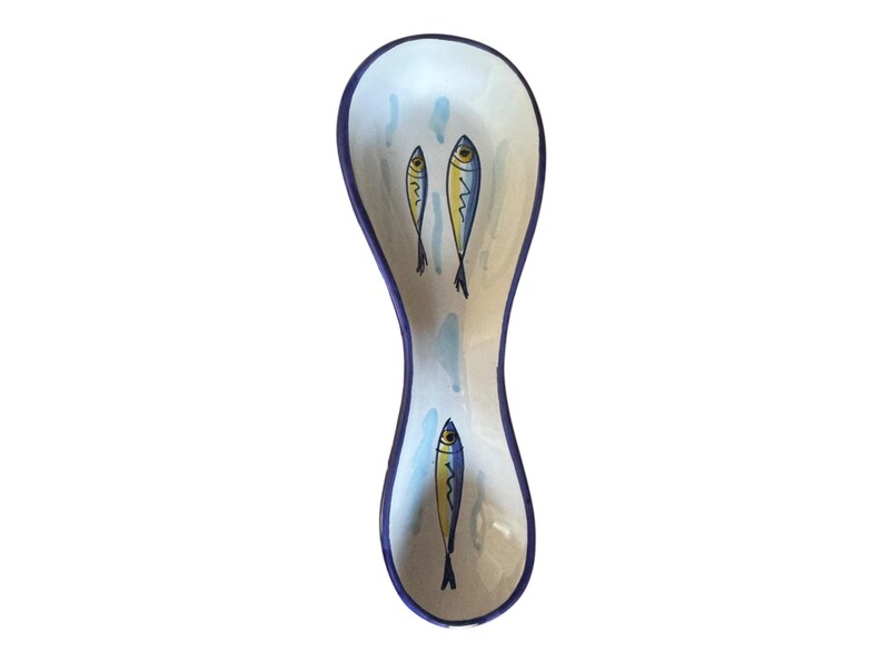 May include: A ceramic spoon rest with a white interior and a blue rim. The spoon rest is decorated with three stylized fish in yellow and blue, with blue water droplet accents.