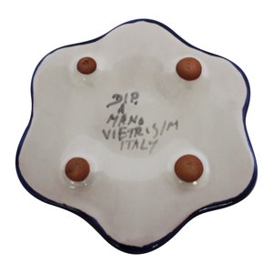 May include: A white ceramic dish with a blue rim and four brown feet. The bottom of the dish has the text "DIP A MANO VIETRIS/M ITALY" written in black.