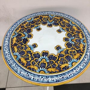 May include: Round white table top with a blue and gold floral design. The table top is made of ceramic and has a white base.