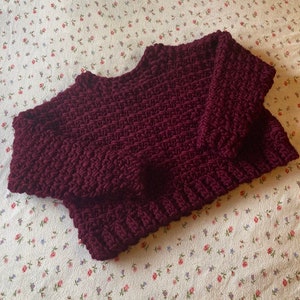 May include: A maroon crocheted sweater with a loose fit and a round neckline.