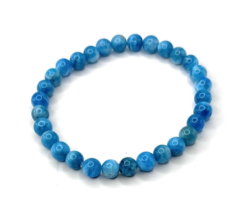 Puede incluir: Un brazalete de cuentas azules. El brazalete presenta cuentas redondas y pulidas en diferentes tonos de azul. Las cuentas est&aacute;n ensartadas en una banda el&aacute;stica, creando un accesorio flexible. El brazalete se muestra sobre un fondo blanco.