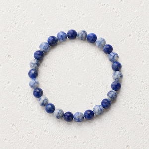 May include: A circular beaded bracelet featuring alternating smooth, round beads in shades of deep royal blue and mottled light blue and white. The beads are strung together in a continuous loop, showcasing a polished finish and a consistent size.
