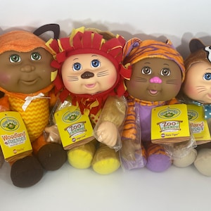 May include: Four Cabbage Patch Kids dolls dressed as animals. The dolls are wearing costumes of a fox, a lion, a tiger, and a skunk. Each doll has a tag with the words "Zoo Friends" or "Woodland Friends".