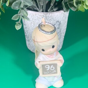 May include: A porcelain figurine of a young angel with blonde hair wearing a halo and holding a chalkboard with the number 96 and the text "Year in School".