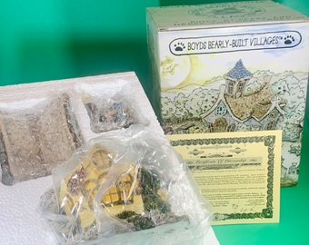 May include: A miniature house with a yellow facade and brown roof, part of a Boyds Bearly-Built Villages collection. The house is packaged in a white foam box with a certificate of ownership.