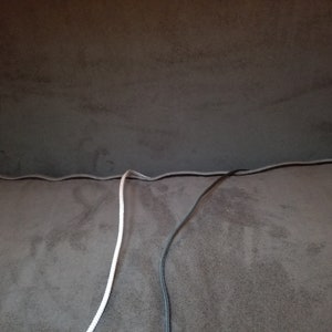May include: Two cords, one white and one black, are seen running along the seam of a brown fabric surface.