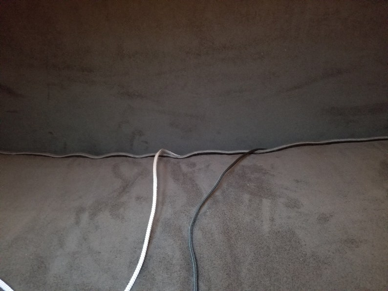 May include: Two cords, one white and one black, are seen running along the seam of a brown fabric surface.