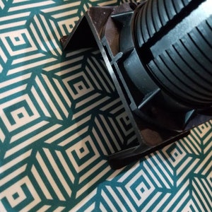 May include: Close-up of a black plastic electrical outlet cover with a ribbed design. The cover is on a white and teal patterned surface.