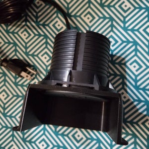 May include: A black electric foot warmer with a cord and plug. The warmer has a rounded base and a curved top.