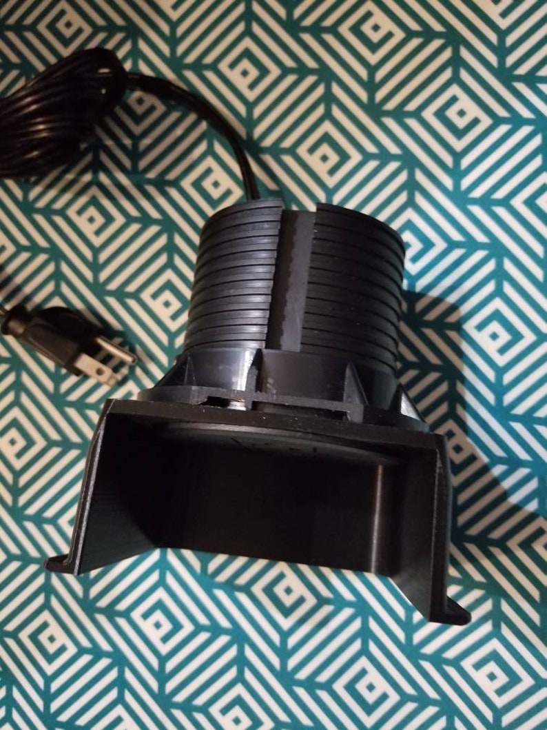 May include: A black electric foot warmer with a cord and plug. The warmer has a rounded base and a curved top.