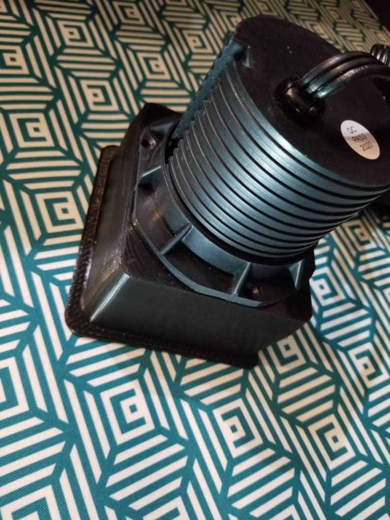 May include: A black, round, electrical device with a series of concentric rings. The device has a black cord and a label that reads "QC PASS 2020".