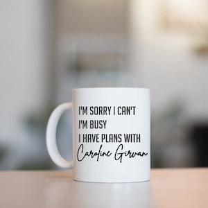 May include: White ceramic coffee mug with black text that reads "I'm sorry I can't I'm busy I have plans with Caroline Girwan".