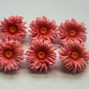 May include: Six individual flower-shaped embellishments arranged in two rows of three. Each piece features layered, textured pink petals radiating outwards from a small, bright yellow centre, creating a realistic floral appearance.
