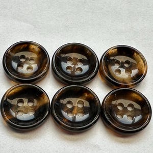 May include: Six round buttons with four holes each. The buttons have a dark brown and amber tortoiseshell pattern. The buttons are arranged in two rows of three on a white surface. These buttons are suitable for sewing projects.