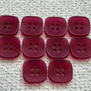 May include: Ten square, translucent, burgundy buttons with four holes each are arranged on a white, textured surface. The buttons have rounded corners and a slightly raised edge. These buttons are suitable for sewing projects.