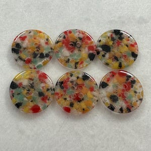 May include: Six round buttons with a colourful speckled design. The buttons feature a mix of red, yellow, green, black, and white specks. Each button has four holes for sewing.