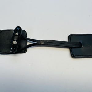 May include: Black leather equestrian equipment, featuring a central black handle and two shield-shaped end pieces. The handle is a glossy, rounded shape. The leather appears smooth and well-maintained.