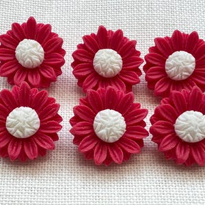 May include: A set of six circular buttons shaped like flowers with vibrant red petals and a textured white centre. Each button features a detailed, raised petal design radiating from the round, white, embossed core, creating a uniform floral appearance.