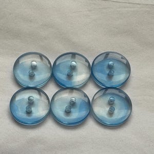 Puede incluir: Seis botones de plástico azul claro con dos agujeros cada uno.