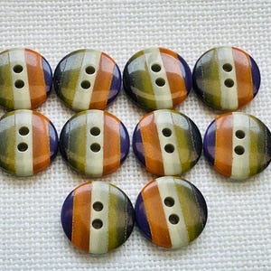 Puede incluir: Diez botones redondos dispuestos en tres filas, cada uno con un patrón de rayas verticales en tonos morado, naranja, verde oliva y crema. Cada botón tiene dos agujeros centrados para su fijación y un acabado liso y brillante.