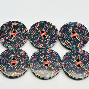 May include: Six round wooden buttons with a dark background and a colorful floral design. The buttons have two holes for sewing and are approximately 1.5 inches in diameter. The floral pattern includes red, yellow, green, and blue accents.