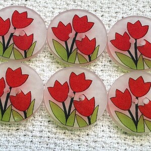 May include: Six circular, translucent buttons with a floral design. Each button features three red tulips with green leaves and black stems. The buttons are set against a white, textured background.