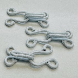 May include: Three white rope toggles, also known as hook and loop fasteners, are shown on a white surface. The toggles are made of a thick, braided rope and have a loop on each end.