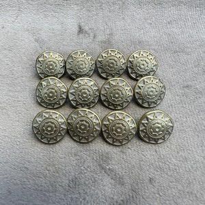 Op de afbeelding: Een set van 12 goudkleurige metalen knopen met een decoratief zonnestralenontwerp. De knopen hebben een reliëf, gestructureerd oppervlak en een zilverkleurige kern.