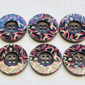 May include: Six round buttons with a swirling pattern in black, pink, and cream. Each button has a dark brown center with four holes for sewing. The buttons are arranged in two rows of three on a white textured surface.