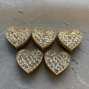 May include: Five gold heart-shaped charms with clear rhinestones. The charms are about 1 inch in diameter.