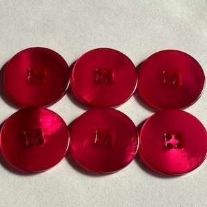 May include: Six round, bright red buttons with a glossy finish. Each button has a square, four-hole design in the centre. The buttons are arranged in two rows of three on a white surface.