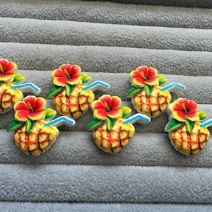 Könnte beinhalten: Sechs bunte Ananas-Getränke-Anhänger mit einer roten Hibiskusblüte und einem blauen Strohhalm. Die Anhänger sind aus Harz und perfekt, um Ihren Bastelarbeiten einen tropischen Touch zu verleihen.
