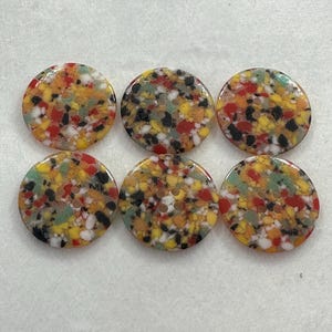 Könnte beinhalten: Sechs runde Knöpfe mit einem gesprenkelten Design in Gelb, Rot, Schwarz, Weiß und Grün. Jeder Knopf hat zwei Löcher zum Nähen. Die Knöpfe sind in zwei Dreierreihen angeordnet.