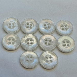 May include: Ten white pearl buttons with four holes each. The buttons are arranged in a circle with the top button at the top of the image.